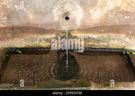 Stone fountain with water jet with moss and smooth stone in horizontal Stock Photo