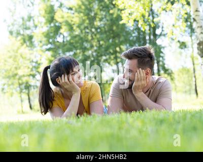 Fun and love concept with mid adult couple lying down in grass looking toeach other and smiling Stock Photo