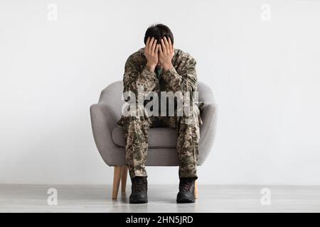 Unhappy man in camouflage sitting at arm chair, copy space Stock Photo