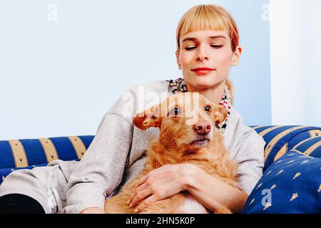 Ginger female sitting on couch and looking down while resting with cute dog with red fur at home Stock Photo