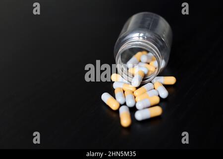 Pills on a dark wooden table, medication in capsules scattered from a bottle. Background for pharmacy, antibiotics, vitamins Stock Photo