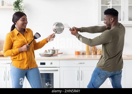 Positive african american couple having fun in kitchen, playfully fighting with kitchenware Stock Photo