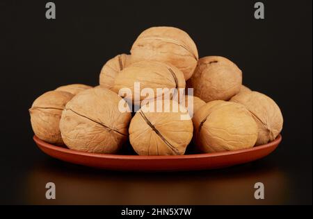 A mound of walnuts on a clay plate on a black background Stock Photo