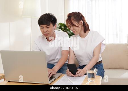 Positive couple managing family finances via form on laptop and filling income tax forms online Stock Photo