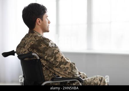 Upset thoughtful soldier sitting in wheelchair, looking through window Stock Photo