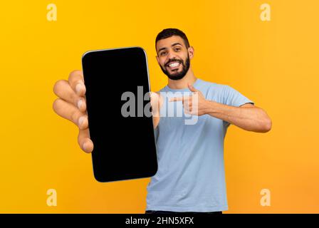 Happy guy presenting smartphone with black screen, pointing at gadget Stock Photo