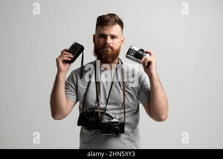 Professional photographer in a grey t-shirt with a bunch of different vintage cameras in a hands and on a shoulder looking on a camera and ready for Stock Photo