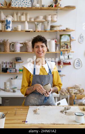 Happy self-employed pottery artist woman in creative studio work with raw clay shaping handmade cup Stock Photo