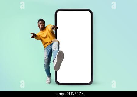 Hey you, check this website. Excited black man standing near huge smartphone with blank screen, mock up Stock Photo