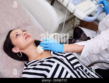 doctor in rubber gloves makes an ultrasound of the thyroid gland of a young pretty woman in a modern clinic. Stock Photo