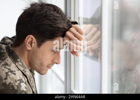 Depressed guy soldier looking through window at home Stock Photo