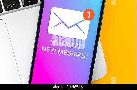 You have new message text notification on a mobile phone screen close-up view. Business communication concept, laptop and office table background Stock Photo