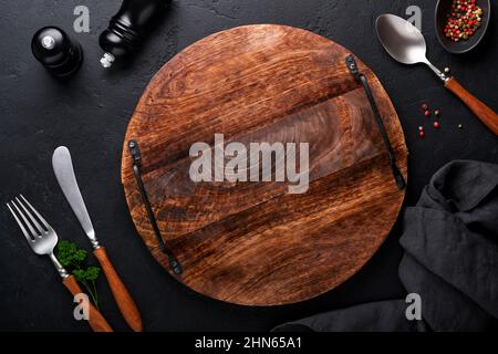 Vintage silverware. Rustic vintage set of wooden spoon and fork on wooden platter on black background. Empty dishes. Top view. Mock up. Stock Photo