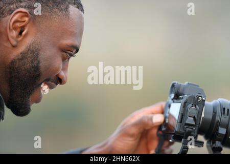 Photographer with black skin checking photos on mirrorless camera screen outdoors Stock Photo