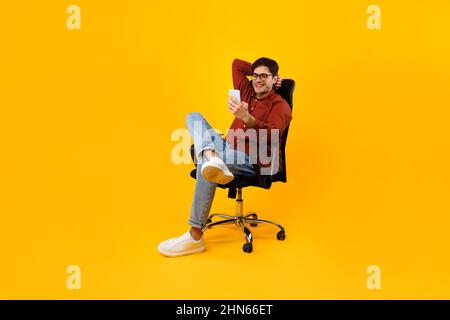 Man Using Smartphone Sitting In Chair Texting Over Yellow Background Stock Photo