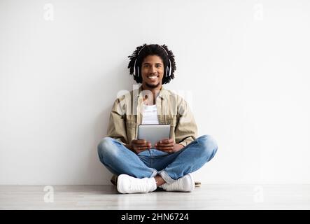 Modern Technologies. Happy Black Guy In Wireless Headphones Using Digital Tablet Stock Photo