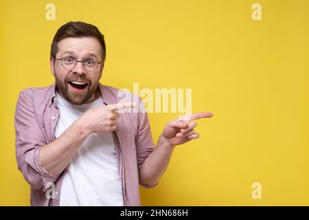 Funny smiling little man in glasses points to something with his index finger and looks joyfully. Copy space.  Stock Photo