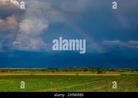 The rainbow over the cultivation fields and the majestic mountains of the Valle del Cauca region in Colombia Stock Photo