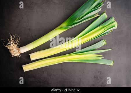 Leek Halved Lengthwise on a Dark Background: Preparing fresh leeks on a dark stone countertop or table Stock Photo