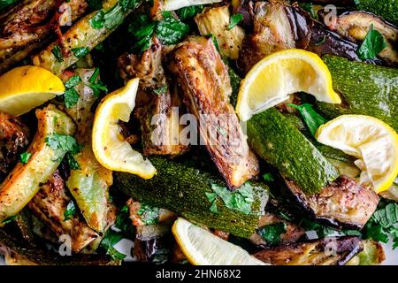 Closeup View of Roasted Aubergine and Courgette with Sumac and Herbs: Close-up of roasted eggplant and zucchini on a sheet pan Stock Photo