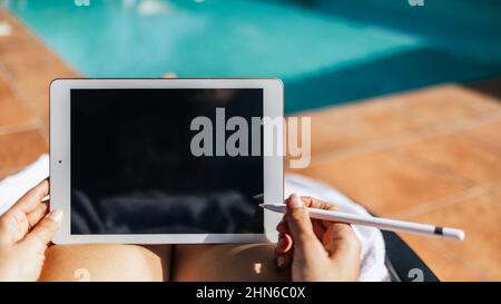 Close up of unrecognizable woman working with a tablet with an electronic pen next to a turquoise pool Stock Photo