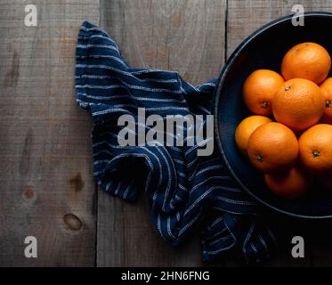 Overhead of bowl of oranges and blue cloth on rustic wood table. Stock Photo