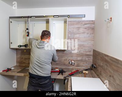 caen, france February 2022. Carpenter assembles kitchen furniture and cabinets. Professional furniture assembly in the kitchen Stock Photo