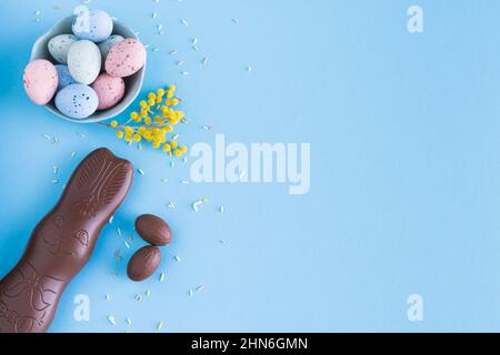 Easter eggs and chocolate bunny on blue background with yellow flower decorations. Top view. Copy space. Stock Photo