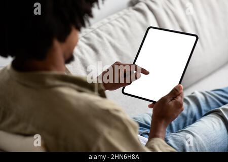 Young Black Man Using Blank Digital Tablet With White Screen At Home Stock Photo