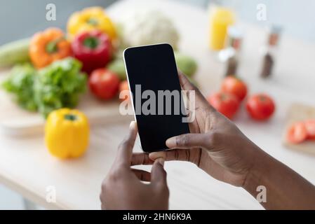 Hands of young african american woman hold smartphone with blank screen making photo on table Stock Photo