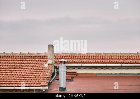 Red bricks roof, metal and concrete made of chimneys and overcast sky background. Stock Photo