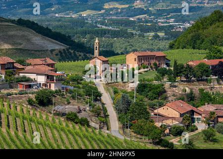 View of rural road through the village and parish church among green vineyards in Piedmont, Northern Italy.