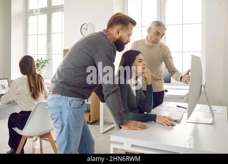Team of employees using computer, working on online project and discussing something Stock Photo