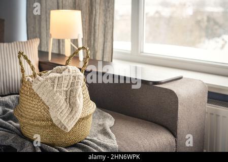 Straw wicker basket with knitting on sofa in interior. Bamboo basket stylish interior item eco design handmade. Decor of home. Stock Photo