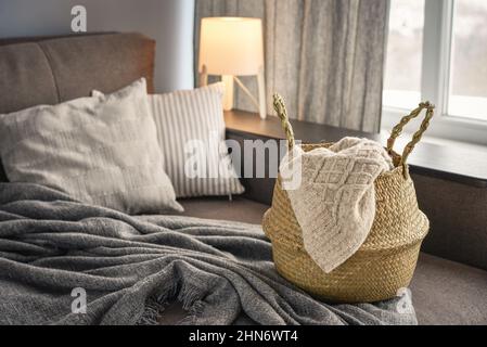 Straw wicker basket with knitting on sofa in interior. Bamboo basket stylish interior item eco design handmade. Decor of home. Stock Photo