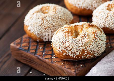 Freshly baked sesame seeded bagels served on a wooden board on a wooden background. Close up. Stock Photo