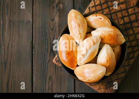 Potato stuffed hand pies - pirozhki in a black bowl on a wooden board. Top view and copy space. Stock Photo