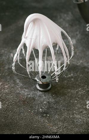 Whipped egg whites - beaten italian meringue on a wire whisk on gray background, copy space. Stock Photo