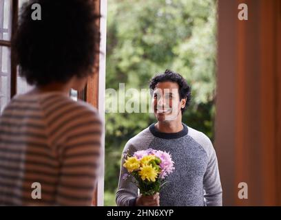 For you...my love. Cropped shot of a young man surprising his wife with flowers. Stock Photo