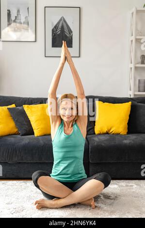 Peaceful and calm senior female practicing yoga at home, an older woman sits in lotus position, middle aged lady meditates. Health and wellbeing concept Stock Photo