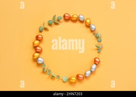 Frame made of Easter eggs and eucalyptus branches on orange background Stock Photo