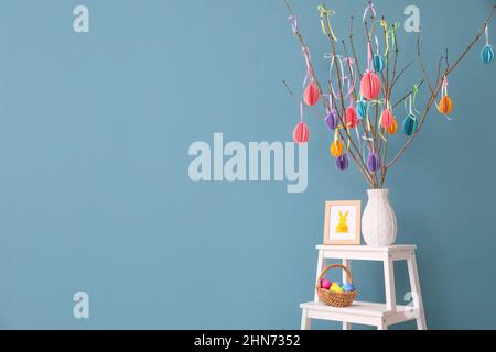Basket with Easter eggs, photo frame and vase with tree branches near color wall Stock Photo
