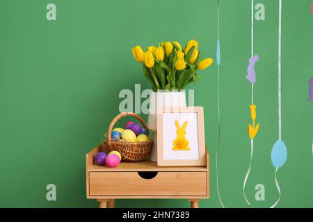 Bouquet of tulips, photo frame and basket with Easter eggs near color wall Stock Photo