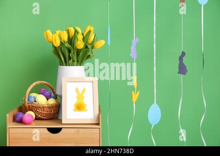 Bouquet of tulips, photo frame and basket with Easter eggs near color wall Stock Photo