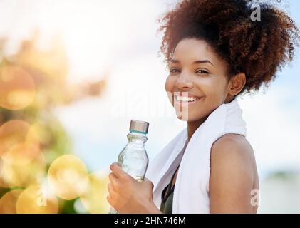 Drink water to replace the fluids you lose while sweating. Cropped shot of a young woman enjoying a bottle of water while out for a run. Stock Photo