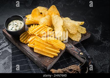 Delicious Potato chips - Crinkle, homemade, hot BBQ on a wooden board. Black background. Top view Stock Photo