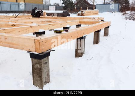 Corner of concrete pile foundation with floor board from square-sawn timber, several carpenters working at frame house Stock Photo