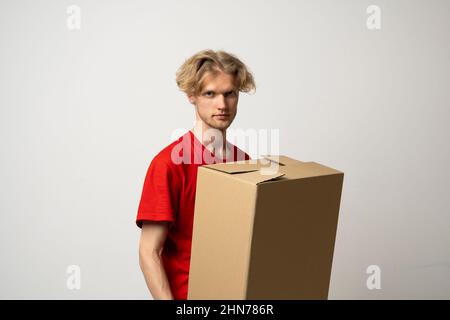 Cheerful delivery man holding a cardboard boxes and smiling while standing against white background. Courier holding a cardboard box in front of Stock Photo