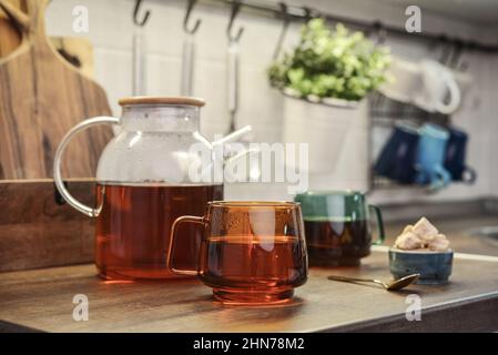 Glass teapot full of black tea with two cups of tea on kitchen worktop closeup Stock Photo