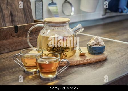 Blooming flowering tea in glass teapot and two cups on kitchen worktop closeup Stock Photo